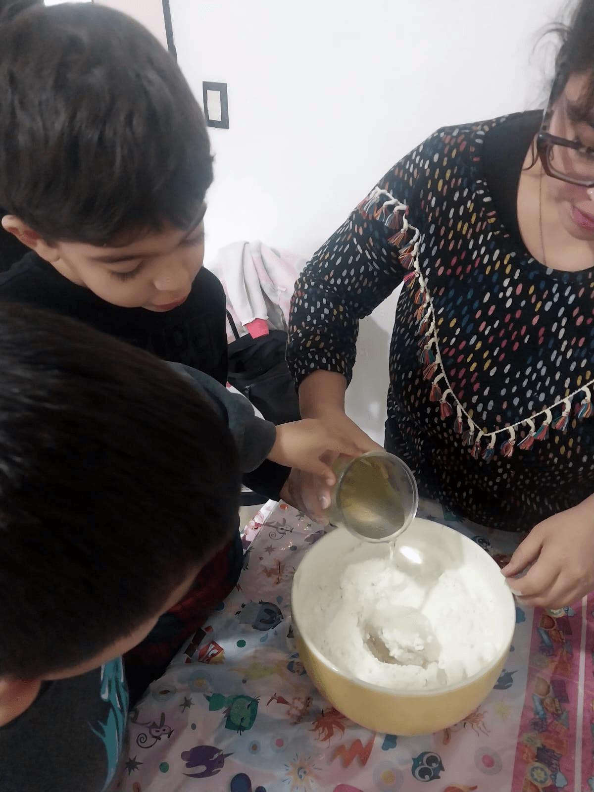 Niños cocinando junto a una educadora, volcando agua sobre la harina en un bol.
