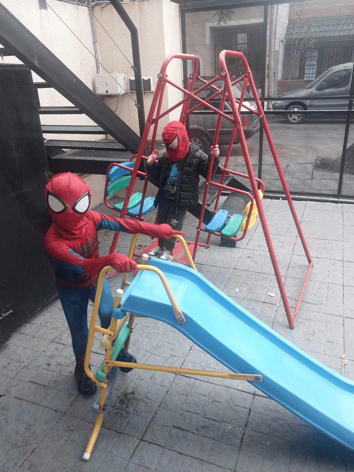 Dos niños disfrazados de Spider-Man jugando en el tobogán y la hamaca del patio.